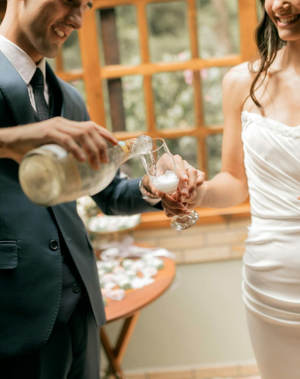 Un marié versant du champagne dans la flûte de la mariée lors de leur réception, une sélection de bulles par vins-mariages.net.