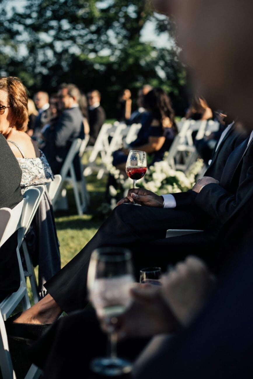 Invité tenant un verre de vin rouge lors d'une cérémonie de mariage en extérieur, servi par vins-mariages.net.