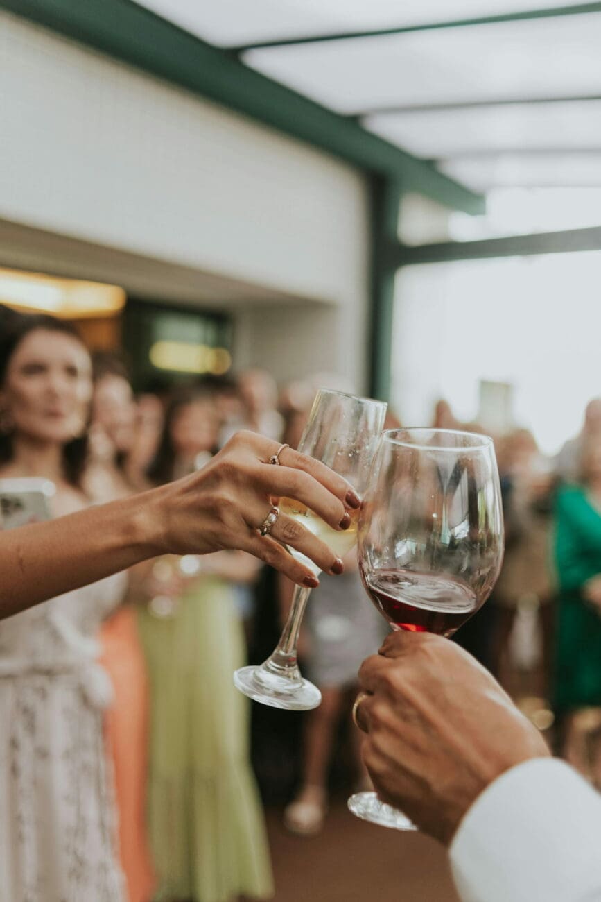 Invités de mariage trinquant avec un verre de vin rouge et une flûte de champagne sélectionnés par vins-mariages.net lors d'une réception.