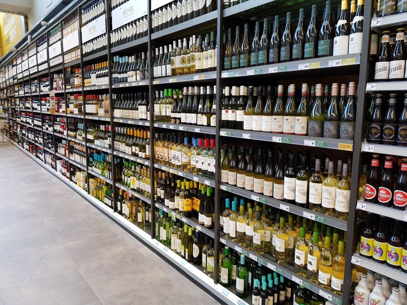 Immense linéaire de bouteilles de vin blanc et de bières dans les rayonnages d'un supermarché.