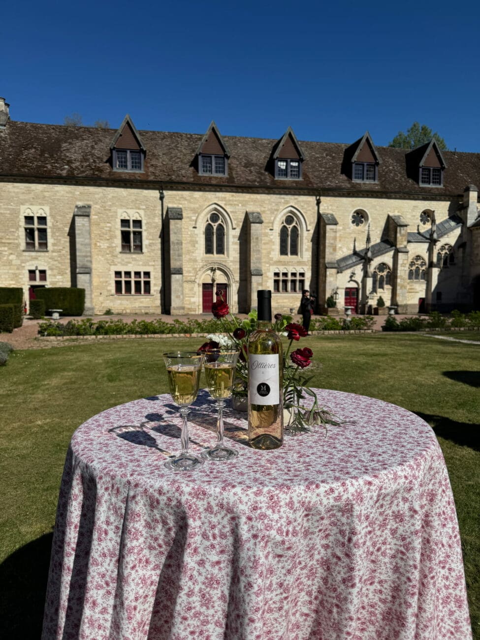 Bouteille de vin rosé Château d'Ollières x Maison Chaperon et deux verres sur une table de mariage devant un château.