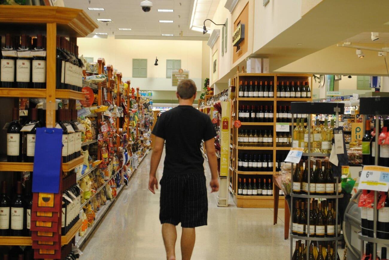 Homme de dos marchant dans le rayon vin d'un supermarché de la grande distribution.